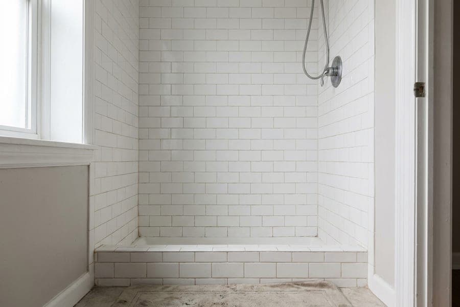 A white subway tile shower wall with a chrome fixture and a low threshold.